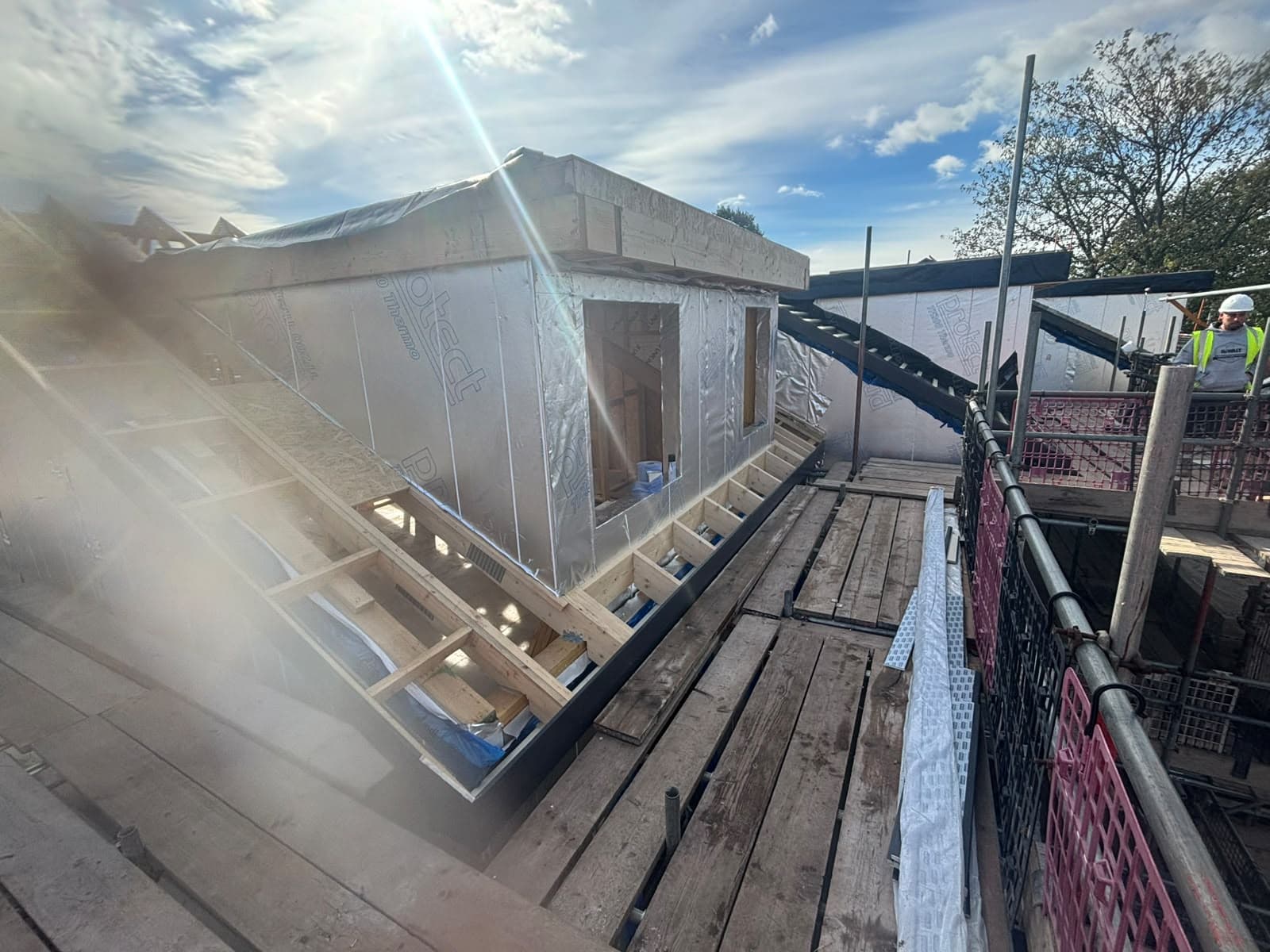 Roof framing and wrapped panels viewed from scaffolding
